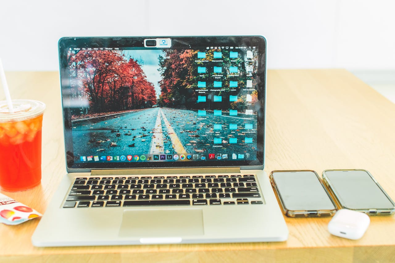A modern setup with a laptop, smartphones, and iced tea on a wooden table indoors.